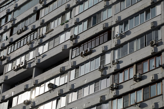 A concrete building facade with many windows and air conditioners
